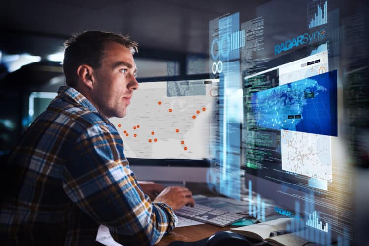 man in office setting monitoring volumes of information coming in from several digital screens